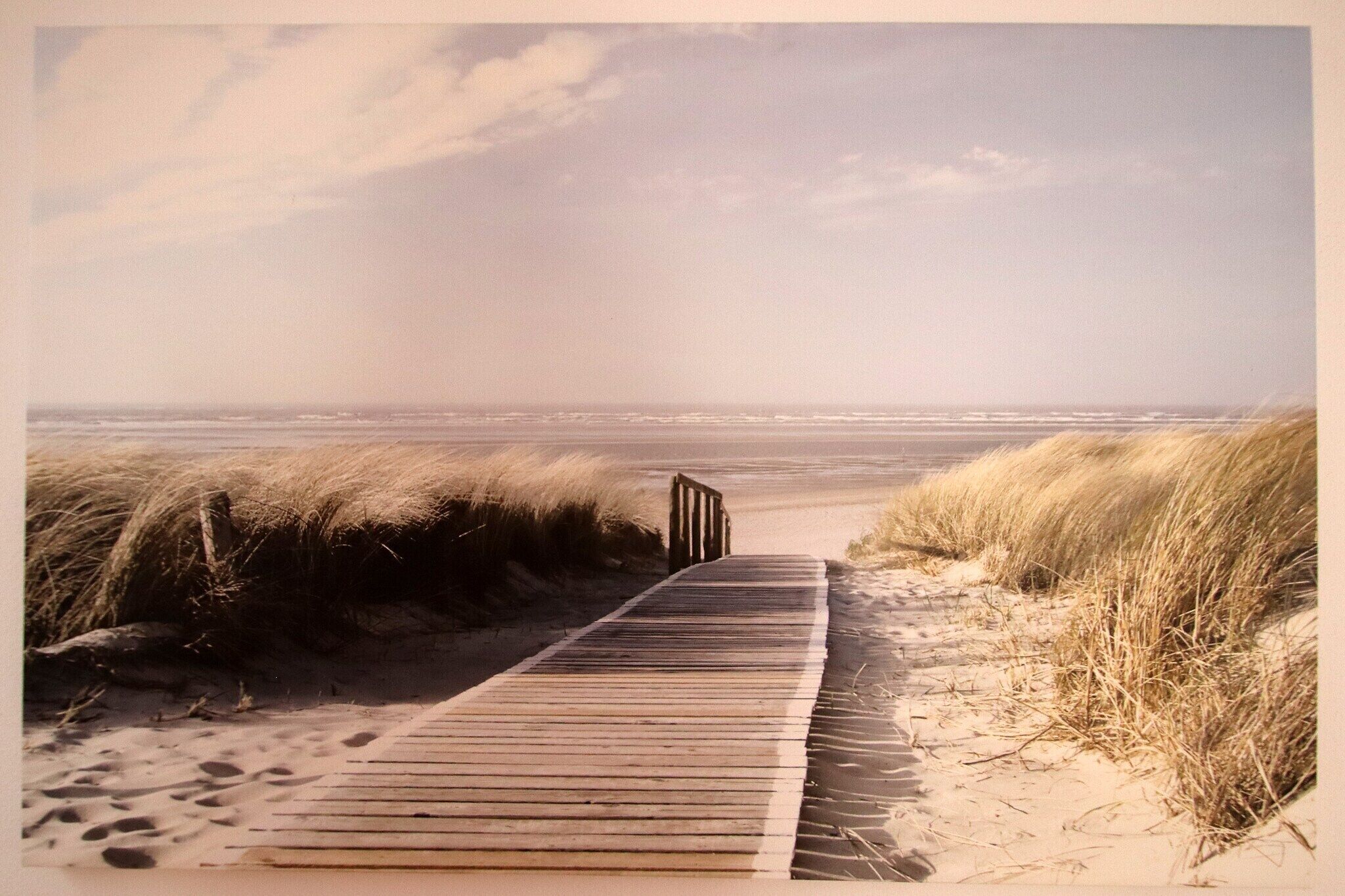 Ein hölzerner Steg führt zu einem Strand mit Dünen und einem klaren Himmel.
