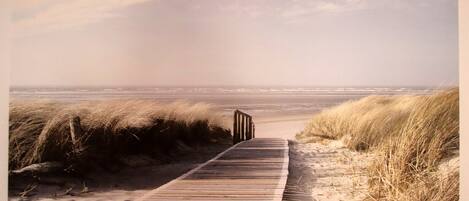 Une promenade en bois qui mène à une plage bordée de dunes de sable, sous un ciel dégagé.