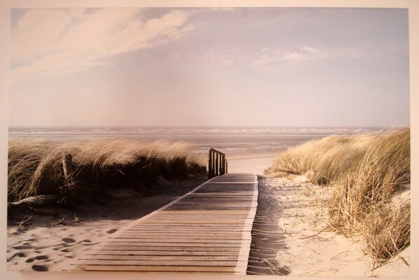 A wooden boardwalk leading to a beach with sand dunes and a clear sky.