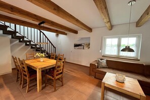 A dining area with a wooden table and chairs, a staircase, a sofa, and a window with a view.