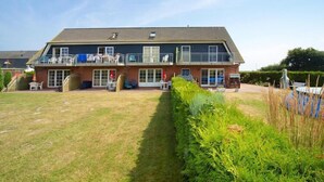 A two-story building with a flat roof, large windows, and a balcony with outdoor seating.