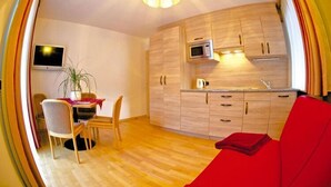 Een ruimtelijk ingerichte leefruimte met een kitchenette, een eethoek en een rode bank.