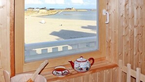 En træhytte med et vindue der kigger ud over en strand, en tepotte og en kop på en hylde.