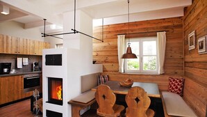 Interior acollidor d'una cabana amb una llar de foc, parets de fusta, una zona de menjador amb cadires i una cuina amb electrodomèstics moderns.