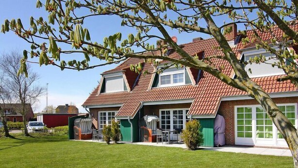 Une maison à deux étages avec un toit recouvert de tuiles rouges, un garage vert et une pelouse bien entretenue.