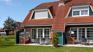 Une maison à deux étages avec un toit recouvert de tuiles rouges, une terrasse couverte avec des meubles d’extérieur et une antenne parabolique.