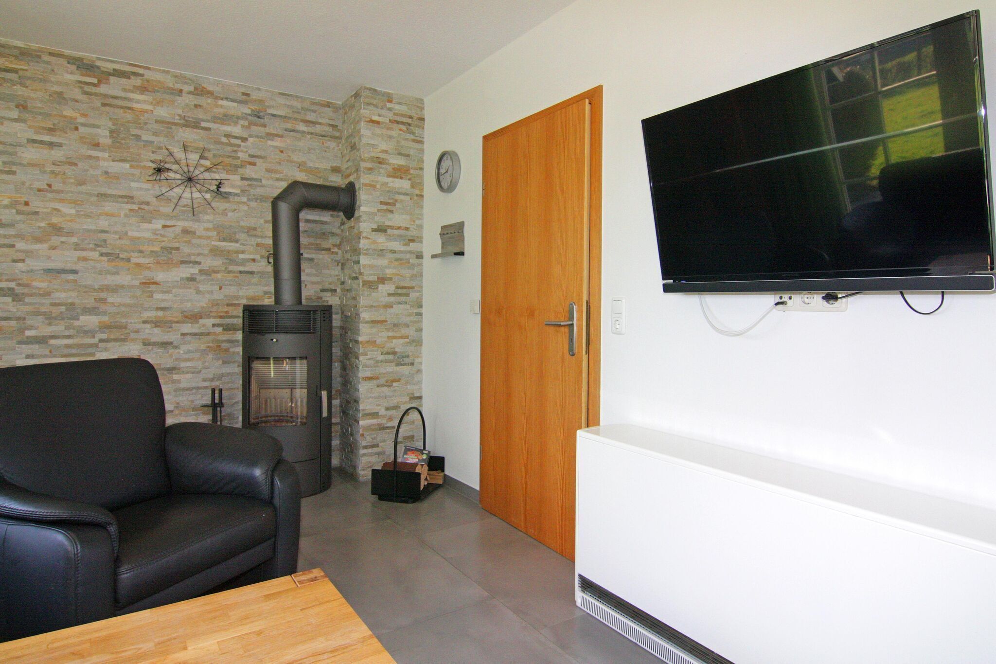 A living room with a stone wall, a black leather sofa, a fireplace, a television, and a wooden door.