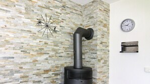 Une pièce moderne avec un mur décoré d’un motif imitant la pierre, un poêle en bois noir, une horloge murale et une œuvre d’art représentant une toile d’araignée décorative.