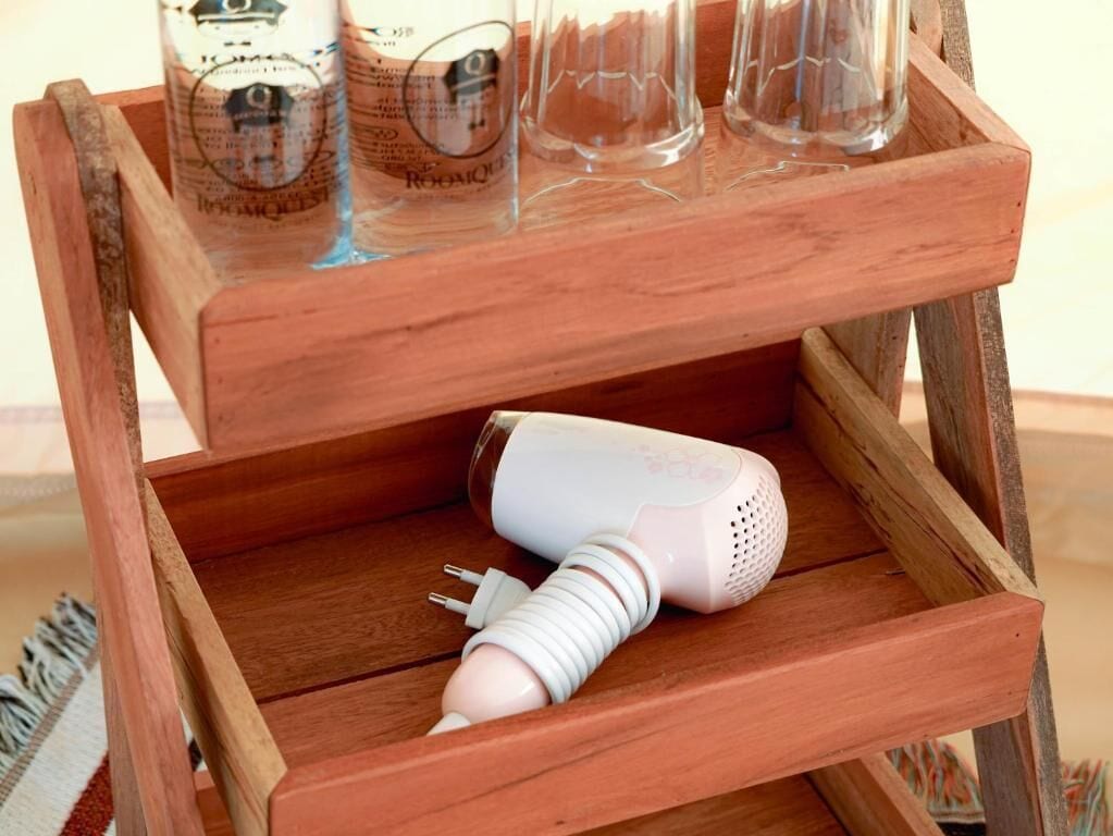 A wooden side table with a hairdryer and three bottles on top.