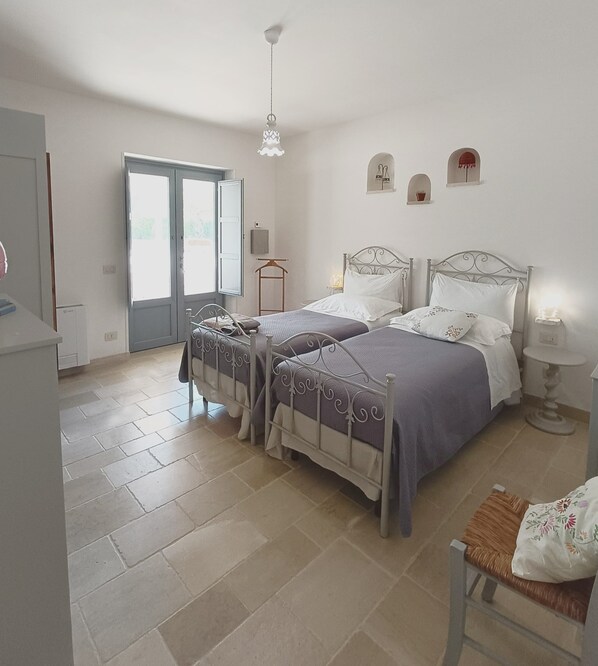 Un dormitorio con dos camas, un armario, una silla, una mesita de noche y una ventana.