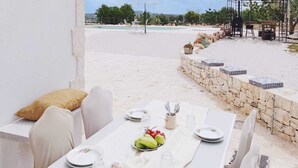 Een terras met een stenen muur, een witte tafel gedekt voor twee personen, en uitzicht op strand en zee.