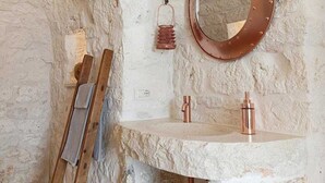 Een rustieke badkamer met een stenen muur, een ronde spiegel, een houten ladder en koperen details.