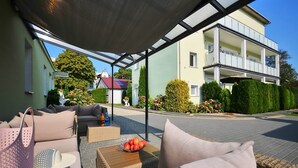 Een overdekt terras met rieten meubilair, een mand appels en een tas.