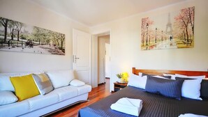 A hotel room with a bed, a sofa, and two paintings on the walls.