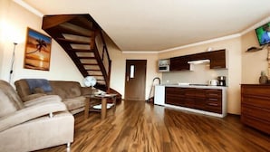 Una sala de estar moderna con una escalera de madera, un sofá, una mesa de centro y una zona de cocina con armarios y un televisor.