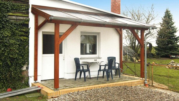 A covered patio with a table and chairs, a brick chimney, and a white building with wooden beams. - Ferienhaus, Parmen bei Feldberg (Parmen)