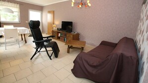 A living room with a sofa, a black chair, a wooden table, a TV, and a bookshelf. - Ferienhaus, Parmen bei Feldberg (Parmen)