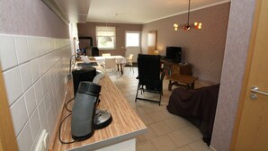 A compact kitchen with a coffee machine, a dining area with a table and chairs, and a television in the background. - Ferienhaus, Parmen bei Feldberg (Parmen)