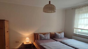 A bedroom with two single beds, a wooden wardrobe, a bedside table with a lamp, and a window with curtains. - Ferienhaus, Parmen bei Feldberg (Parmen)