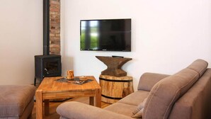 A living room with a sofa, a wooden coffee table, a television mounted on the wall, and a wood-burning stove.