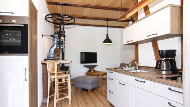 A kitchen with wooden cabinets, a built-in oven, a coffee maker, and a television on the wall.