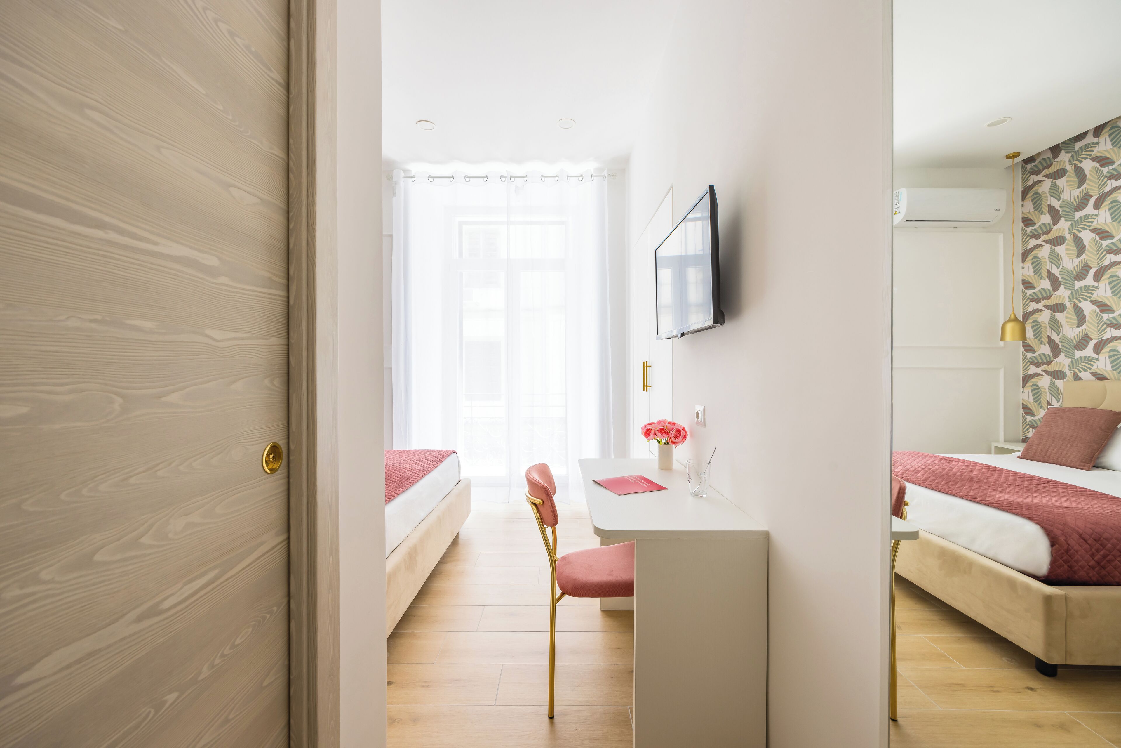 Habitación de hotel moderna con puerta de madera, escritorio con silla, cama con ropa de cama roja y televisor en la pared.