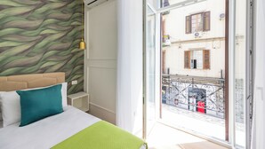 A hotel room with a bed, a green pillow, a patterned wall, and a balcony with a view of the street. - 4 Stelle Housing - Rooms and Apartments by Wonderful Italy (Naples)