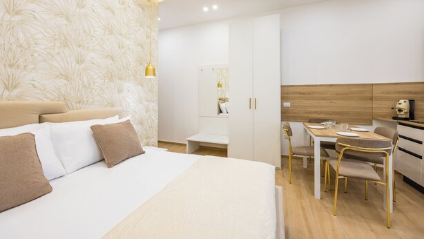 A modern hotel room with a large bed, a dining area with a table and chairs, and a kitchenette. - 4 Stelle Housing - Rooms and Apartments by Wonderful Italy (Naples)