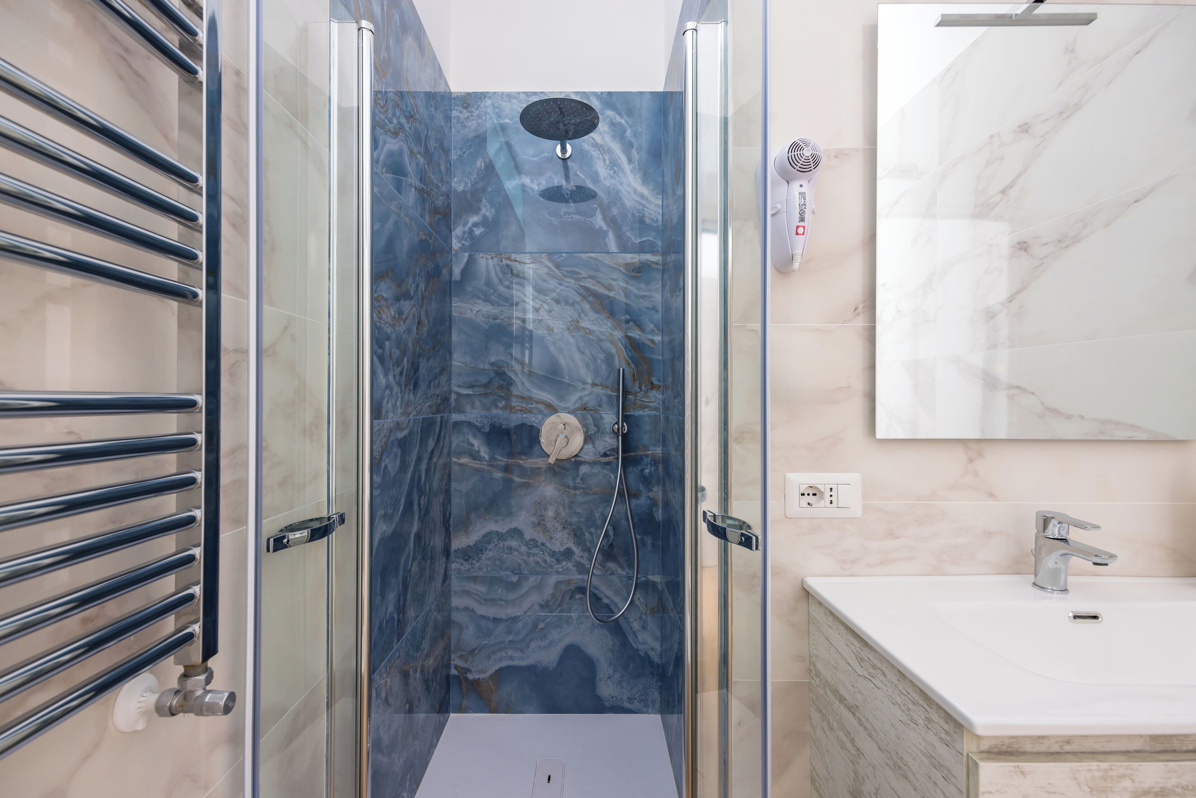 A bathroom with a glass-enclosed shower, a white sink, and a marble-tiled wall.