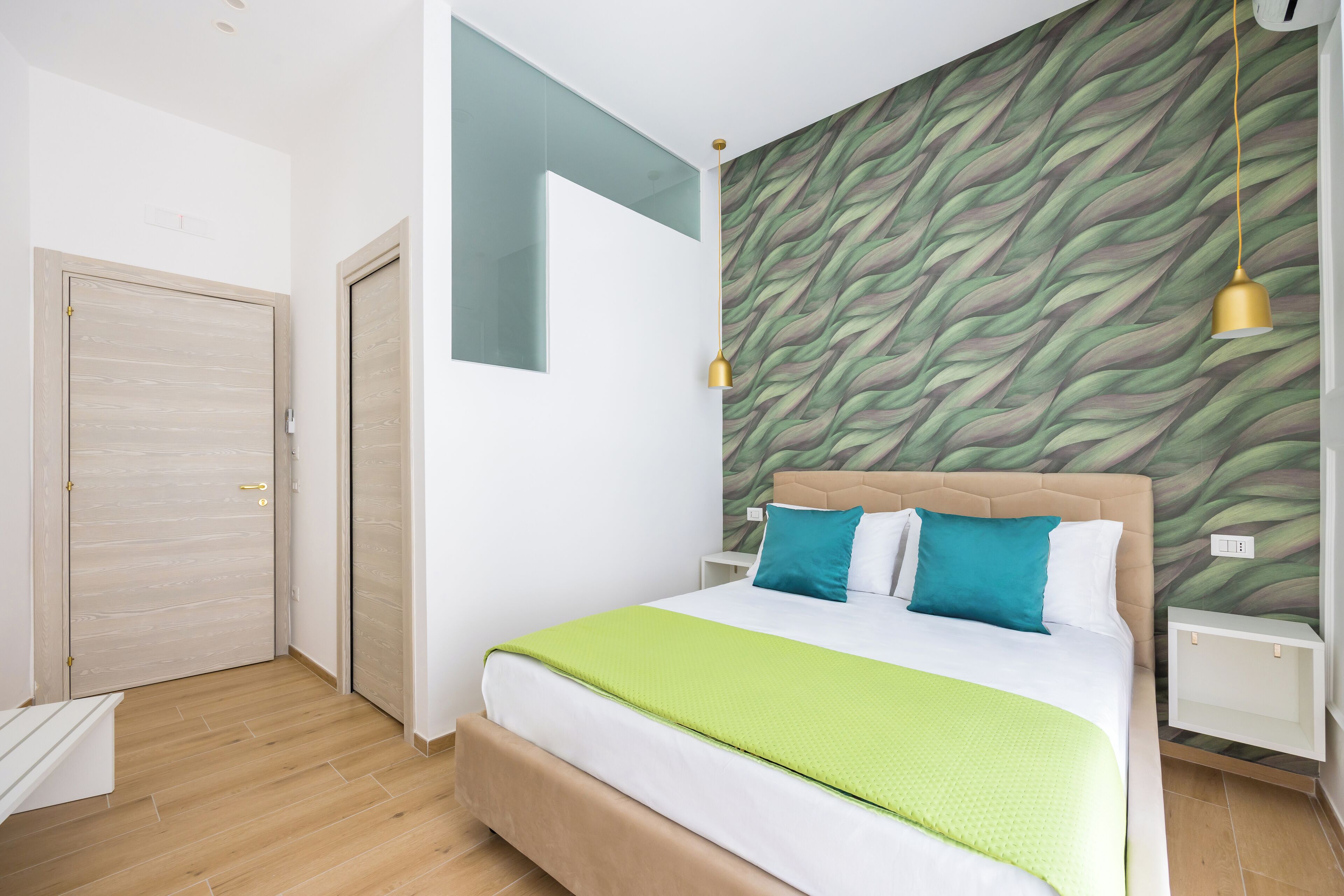 A bedroom with a bed, a nightstand, a wall-mounted light fixture, and a door.