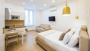 A modern hotel room with a bed, a sofa, a dining area with a table and chairs, a TV, and a kitchen area with a microwave. - 4 Stelle Housing - Rooms and Apartments by Wonderful Italy (Naples)