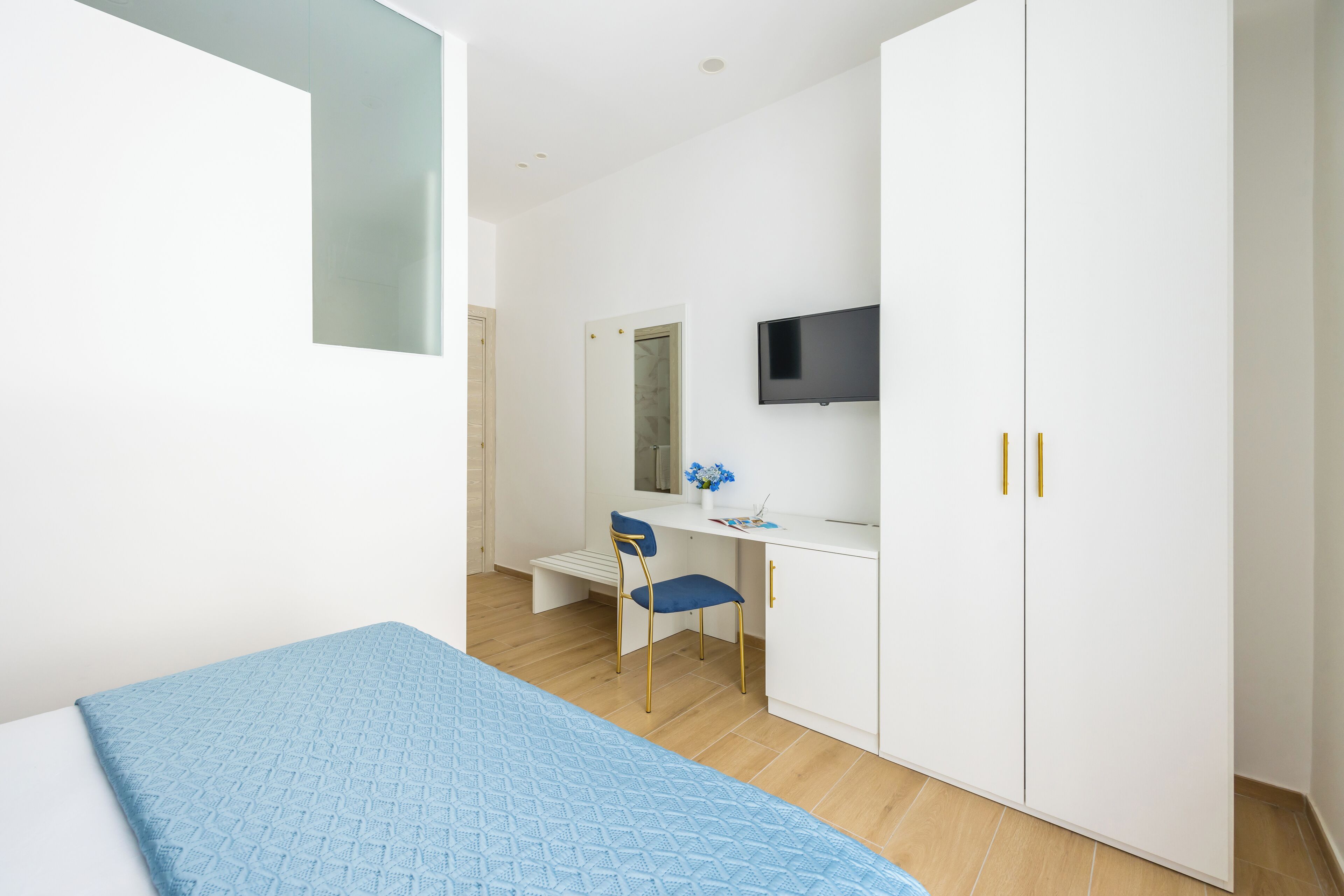 A bedroom with a bed, a desk, a chair, a wardrobe, and a TV.