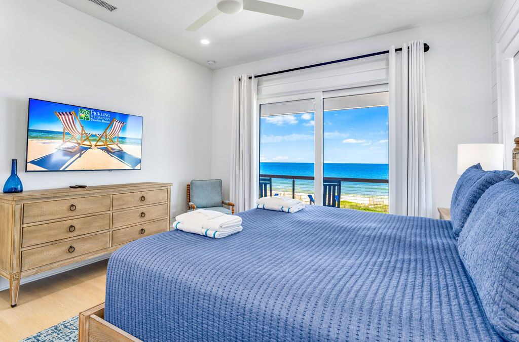 A bedroom with a large bed, a wooden dresser, a television, and a view of the ocean.
