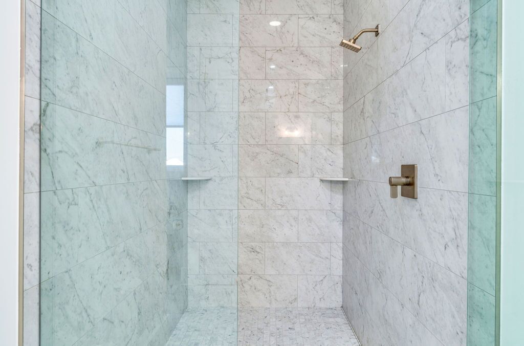 A modern shower with marble walls and a glass enclosure.