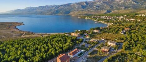 An aerial view of a coastal village with a lake, surrounded by mountains.