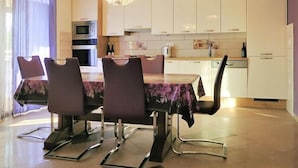 Una cocina moderna con armarios blancos, horno empotrado y microondas. Hay una mesa de comedor con cuatro sillas y una araña colgante.