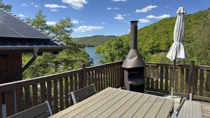 Una terraza con mesa y sillas, una parrilla de barbacoa y vistas a un río y un bosque.