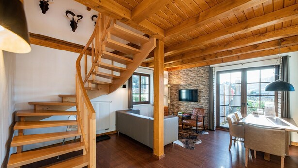 Amplia sala de estar con escalera de madera, chimenea de piedra y un gran ventanal con vistas al exterior.