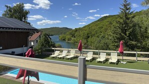 Un espace aménagé au bord de la piscine, avec des chaises longues et des parasols, offrant une vue sur un lac et des collines boisées.