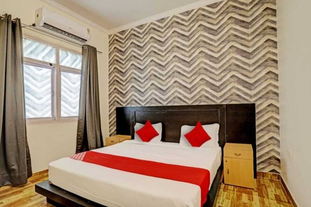 Ein Hotelzimmer mit Bett, Nachttisch, Fenster mit Vorhängen und einer Wand mit Muster.