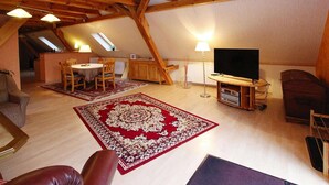 Un loft spacieux avec de hauts plafonds, des poutres apparentes, un coin repas agrémenté d’une moquette rouge, un téléviseur et un coin salon confortable.