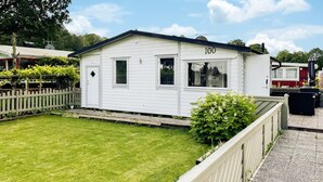 Une maison mobile blanche, avec le numéro « 100 » peint sur le côté, un petit jardin devant et un chemin de gravier.