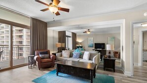 A spacious living room with a large sofa, a coffee table, and a ceiling fan. There is a balcony with a view of a building. - Oceanfront Paradise Perfection 2BR Condo/ Balcony (North Myrtle Beach)