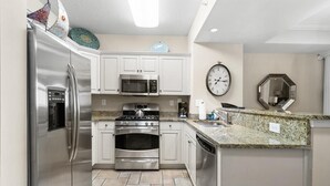 A modern kitchen with stainless steel appliances, white cabinetry, a granite countertop, and a wall clock. - Oceanfront Paradise Perfection 2BR Condo/ Balcony (North Myrtle Beach)