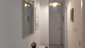 Een gang met een witte deur aan het einde, een spiegel met decoratief kader en een hanglamp.