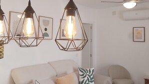 Een woonkamer met een bank, een stoel en hanglampen met zichtbare gloeilampen.