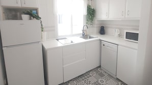 Een keuken met witte kastjes, een spoelbak, een magnetron en een vaatwasser.