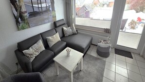 A living room with a black sectional sofa, a white coffee table, and a grey rug.