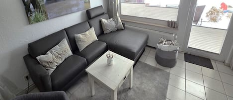 Ein Wohnzimmer mit einem schwarzen Ecksofa, einem weißen Couchtisch und einem grauen Teppich.