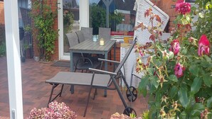 An outdoor patio with a table and chairs, a glass door leading inside, and a brick wall.